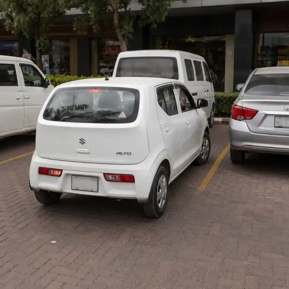 White Suzuki Alto parked in a parking lot during a driving lesson by The Dreamial Driving School in Bahria Town Lahore.